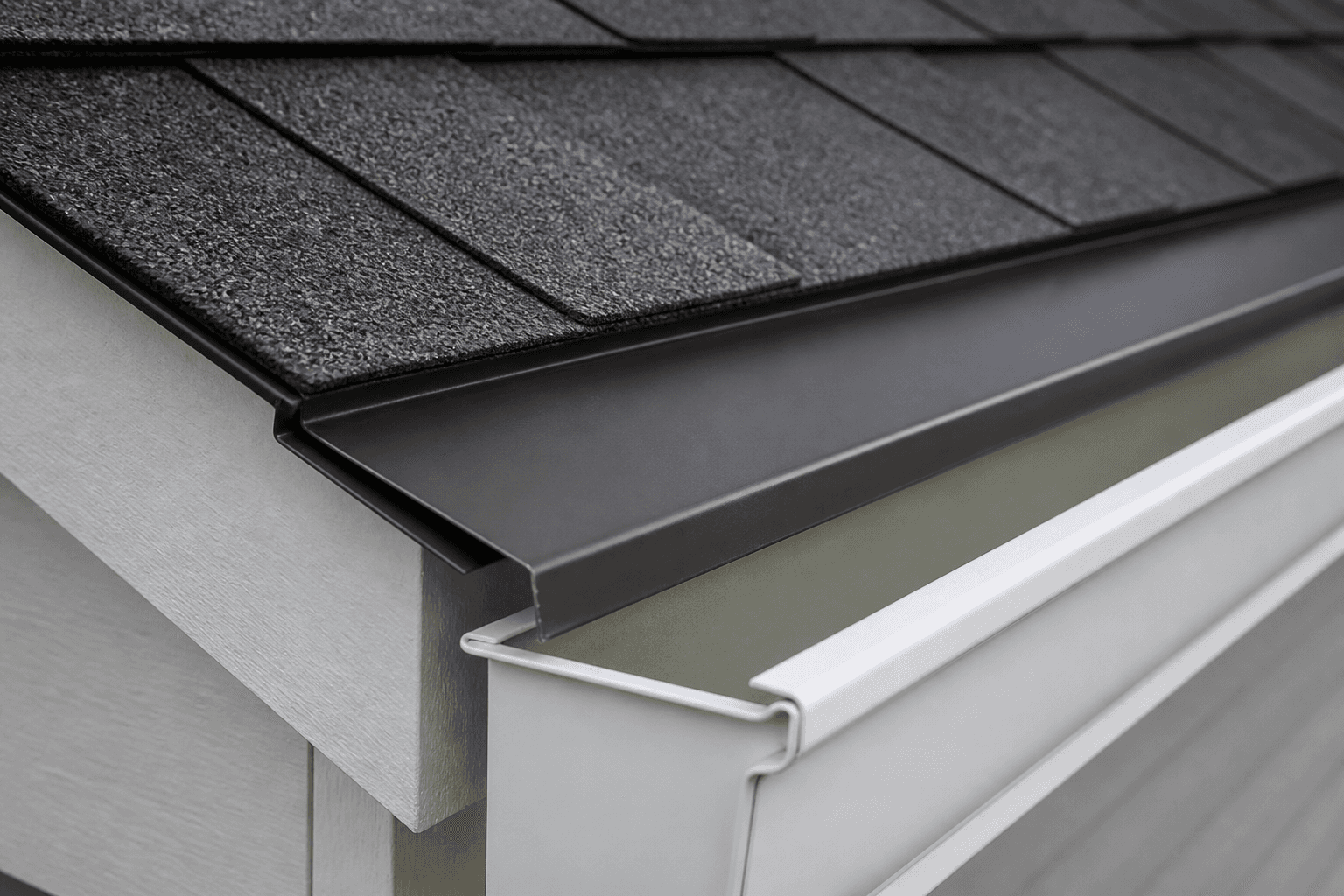 Bronze metal drip edge directing water into a white gutter under charcoal shingles